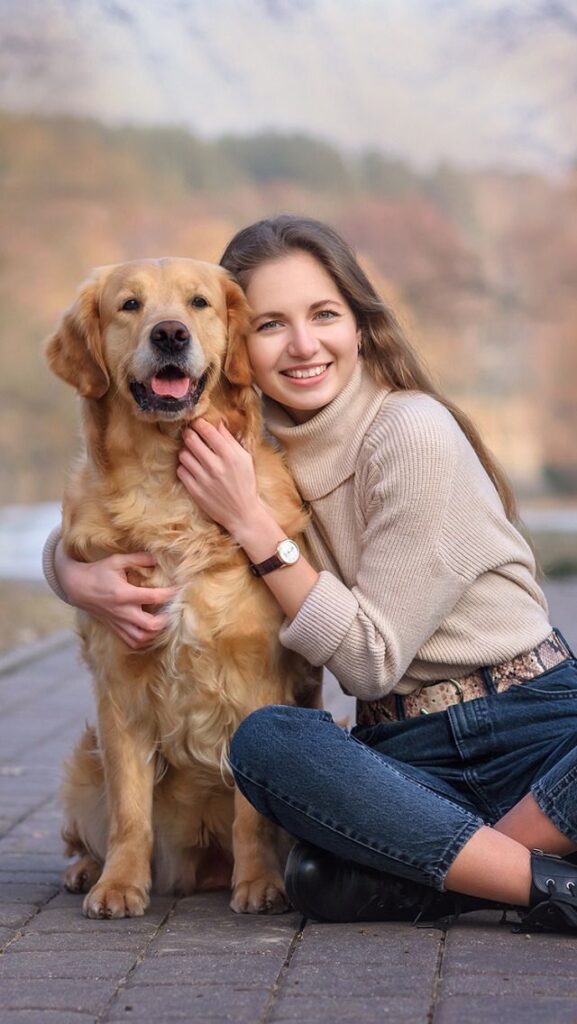 A woman hugs her senior golden retriever outdoors, both smiling in a warm autumn setting, symbolizing the bond between pet and owner during golden years